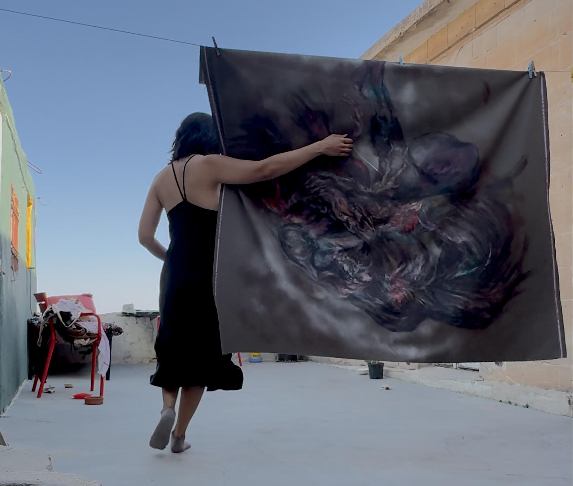 Sinur holding a large painted fabric work outdoors.